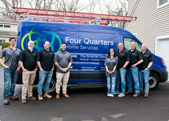 Eight people stand in front of a blue Four Quarters Home Services van in a driveway, all wearing company shirts and jeans or work pants.